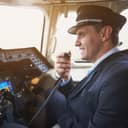 A smiling male pilot in the cockpit of an airplane, conversing through a portable radio set.