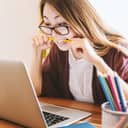 A woman biting a pencil while reading something on her laptop