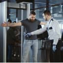 A security agent at an airport conducts a pat-down on a bearded male passenger after he passes through the metal detector scanner in the departures hall.
