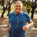 close-up of a smiling senior man in fitness attire running in a park and listening to music