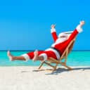 A man dressed as Santa Clause sitting in chair and cheerfully sunbathing at beach near ocean