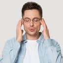 A young man with his eyes closed, slowly exhaling trying to calm himself down
