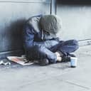 Homeless man sitting on the street in the shadow of the building and begging for help and money. Problems of big modern cities.
