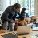 A team lead talking with an employee sitting at the desk and looking at his tablet