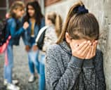Sad elementary age schoolgirl covering her face next to her peers