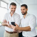 Two businessmen talking in the office, checking information together on a smartphone.