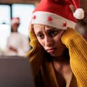 Close-up of a stressed woman wearing a Santa hat while working on her laptop in the office.
