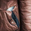 Close-up view of a brown, ripped old jacket above the pocket, with wool stuffing.