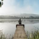 back view of a woman meditating by a foggy pond on a serene morning