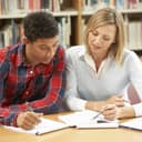 Man and woman sitting next to each other in a library comparing notes on the table