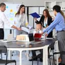 male businessman feeling overwhelmed in a noisy office with colleagues assigning him multiple tasks