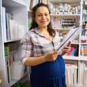 pregnant woman in an art store holding canvases and smiling at the camera