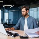 A man focused on his work looking at his laptop while holding a piece of paper
