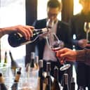 A closeup of a waiter pouring a glass of wine to a guest