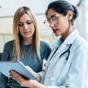 Attentive female doctor explaining treatment details to a female patient using a tablet during a consultation.
