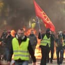 A group of protesters one of whom is wearing a flag with fire burning in the background