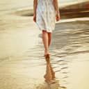 Woman walking barefoot on sand near water