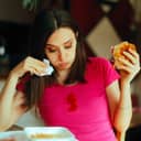 close-up of a woman eating a burger at a restaurant with a ketchup stain on her pink T-shirt