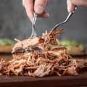 A person making pulled port with two forks on a cutting board
