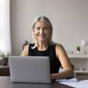 Businesswoman sitting at her desk, working on her laptop and smiling at the camera.