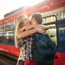 A beautiful couple embraces warmly next to a train, reuniting after being apart for an extended period.