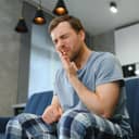 man at home grimacing in pain, holding his hand on his cheek indicating teeth issues