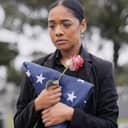 a mourning woman with a rose and flag at a cemetery memorial service