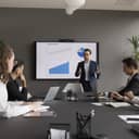 male team-lead conducting a meeting, presenting statistics in a modern conference room with a monitor displaying important information