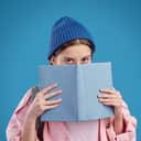 Shy teenager hides her face behind a book.