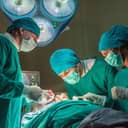 Three experienced surgeons performing a surgery in the hospital, wearing green gowns.