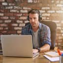 young man listening to music on headphones and working on a laptop at an office desk