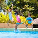 two girls and a boy jumping into an outdoor pool, enjoying summer water fun on a family vacation