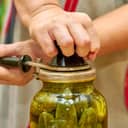 close-up of fresh cucumbers being preserved in glass jars and sealed with a seamer