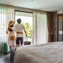 back view of young traveling couple opening the hotel room curtains to enjoy the view