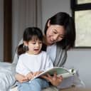 Woman reading a book to a young female child who is sitting in her lap
