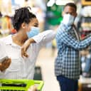 A woman with a mask coughing in a supermarket and a man also with a mask is looking at her