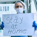 A doctor with a mask, gloves, glasses and a cap holding a Stay at Home sign