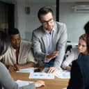 young confident businessman talking to his diverse team of four during an office meeting