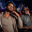 Young people watch a boring movie at the cinema, and one guy is sleeping.