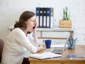 A young woman at an office desk holding her hand over her eyes and yawning
