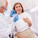 Scared woman sitting in the dental chair as the dentist approaches with a dental drill and angled mirror.