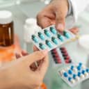 close-up of a male pharmacist's hand giving green prescription pills to his female customer