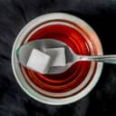 Colse-up of two sugar cubes carefully placed on a teaspoon, above a cup of tea.