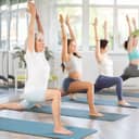 four women performing a yoga pose and stretching in a gym setting