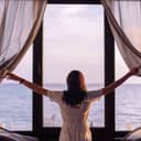 A young woman opening curtains to see the ocean