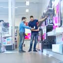 An electronics store worker talking with a potential customer and showing them TVs
