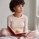 A young woman sitting on a bed in her pajamas writing into her journal