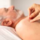 Close-up of a therapist expertly applying needles to the shoulder of an elderly man for therapeutic purposes.