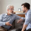 elderly father and adult son sitting on a sofa, engaged in a serious conversation