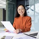 Asian businesswoman in a modern office, confidently holding documents, smiling at the camera